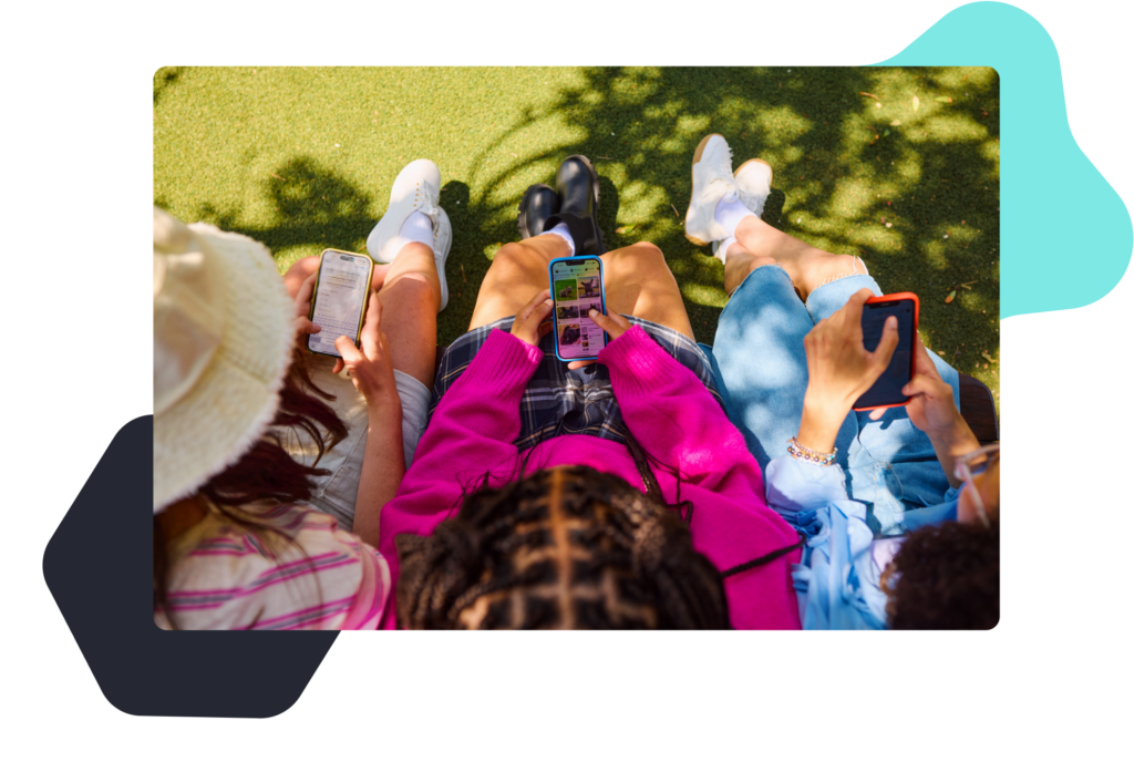 Over the shoulder view of three young people on their cell phones outside on the grass