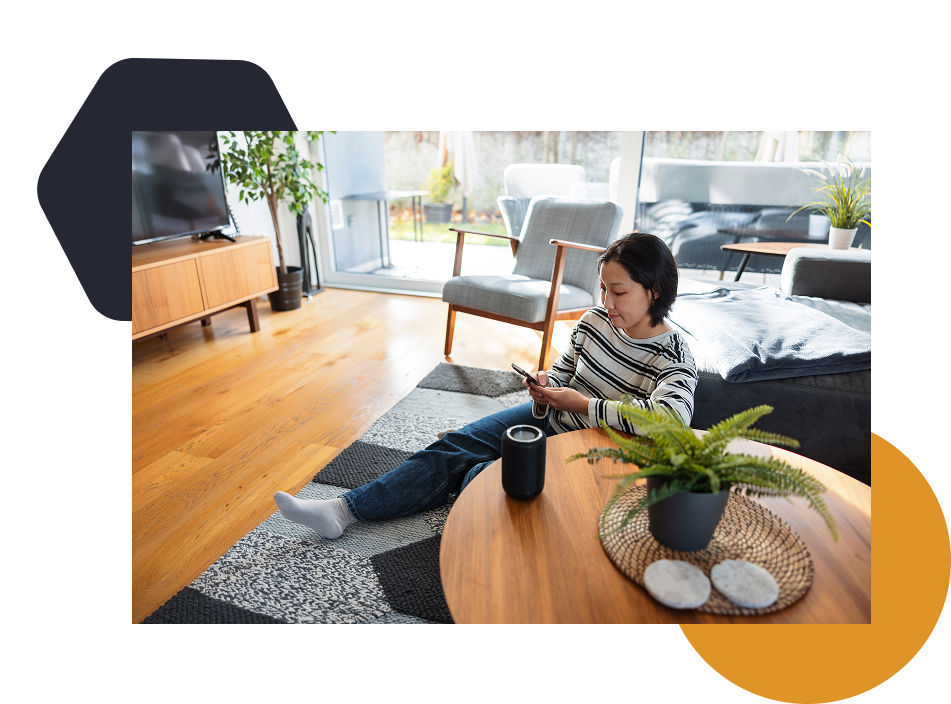 A woman sitting on the floor using a handheld device and a voice activated virtual assistant.